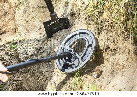 Metal Detector Coil Over A Metal Object Protruding From The Ground. A Shovel Driven Into The Ground 