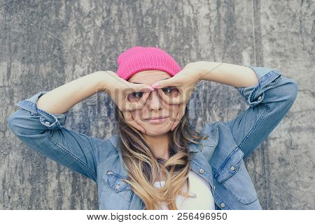 Woman Having Fun. Woman Making Binoculars Using Her Hands. She Is Dressed In Jeand Shirt And Pink Ha