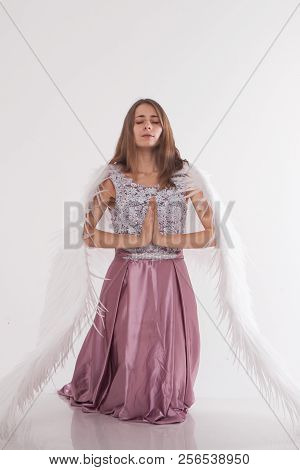 A Beautiful Girl With White Wings Is Kneeling With Her Hands Folded For Prayer. Guardian Angel In Pi