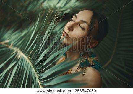 Beautiful Young Woman Posing On A Background Of Exotic Palm Leav