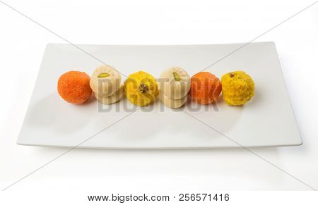 Variety of Indian sweets presented on a modern white platter. Pedha and Bundi Laddu served in a contemporary style.