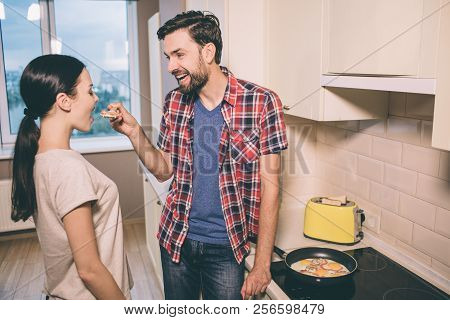 Lovely Pictue Of Man Standing In Front Of Woman And Holding Wooden Spoon With Piece Of Omlet. She Lo
