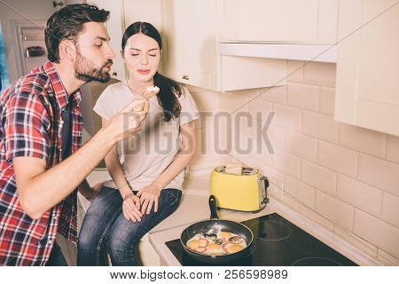 Careful People Are In Kitchen And Cooking Omlet. They Blowing On Piece Of Meal On Wooden Spoon. He H