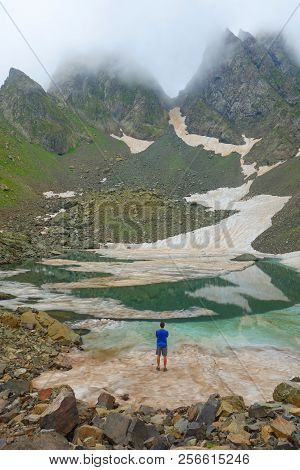 Partially Frozen Didighali Lake With A Young Man And Mountain Pass In The Background In Caucasus Mou