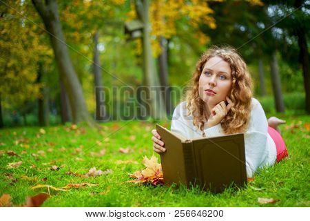 beautiful young plussize woman reading a book   in the autumn park