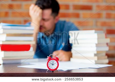 Young Man In Shirt With Books And Alarm Clock On Foreground.