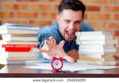 Young Man In Shirt With Books And Alarm Clock On Foreground.