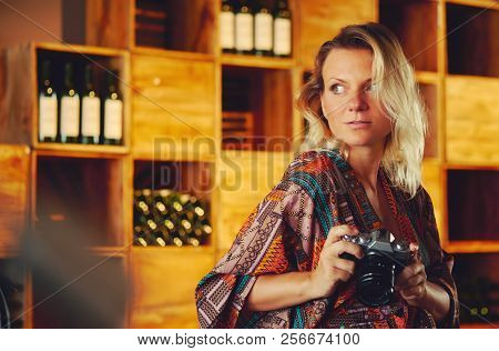 Portrait Of A Young Pensive Blond Woman Holding Photo Camera And Looking Away, Wine Chiller Cabinet 