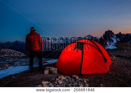 Night bivouac at Tre Cime di Lavaredo, milion star hotel under night sky, red illuminated tent on pass in Dolomites, Italy.