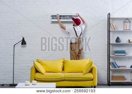 Young Professional Repairman Fixing Air Conditioner Hanging On White Brick Wall