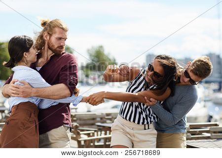 Two girls holding tightly by hands while their boyfriends trying to separate them during double date