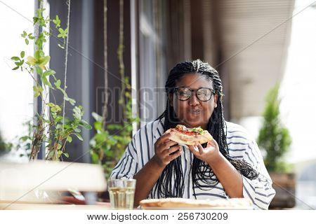 Pleased young woman eating yummy pizza in cafe and enjoying its fantastic taste