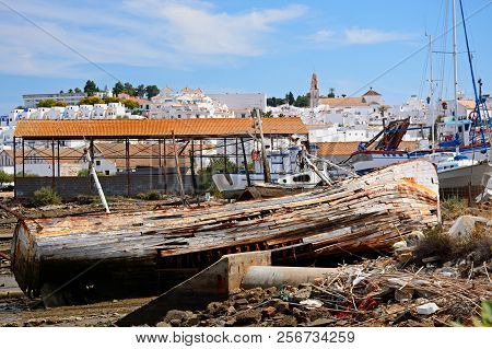 Old Wooden Fishing Boat Ruin On The Riverbank With Views Towards The Town Buildings, Ayamonte, Huelv