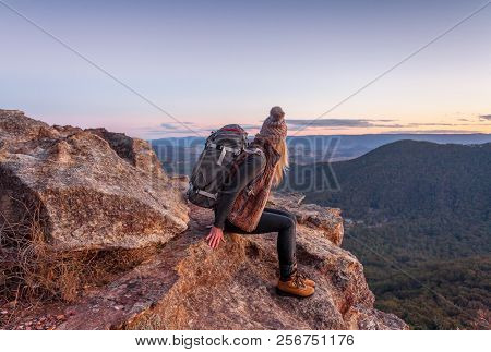 Female Hiker With Backpack Rests On A Mountain Peak Rocky Ledge With Magnificent Views In Blue Mount