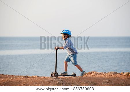 Sport Little Causcasian Boy In Helmet Riding Scooter On Sea Coast In Autumn