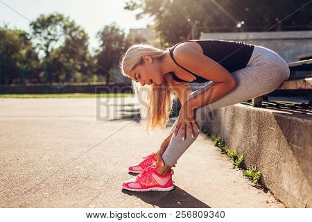 Young Woman Athlete Touching Her Ankle After Running On Sportsground In Summer. Injury During Traini