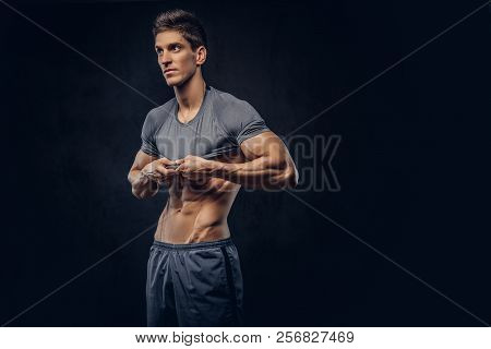 Stylish Ectomorph Bodybuilder With Stylish Hair Takes Off His Shirt On The Dark Background.