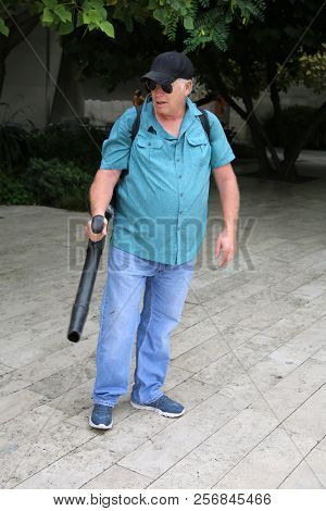 Man uses a Leaf Blower. A man uses a leaf blower to clean up a garden and patio grounds.