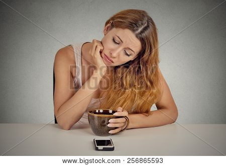 Sad Young Woman Sitting At Table Drinking Coffee Looking At Her Mobile Phone