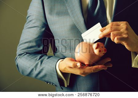 Male Hands Putting Blank Business Card In Piggy Bank For Saving On Grey Background. Fashionable Form