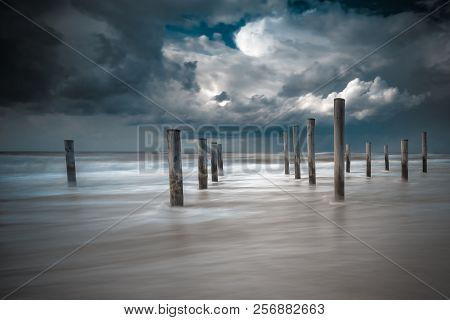 Long Shutter Photo Of Wooden On Sandy Beach With White Clouds And Waves Of The North Sea