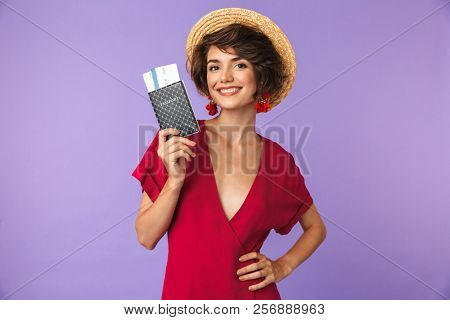 Photo of charming young woman 20s wearing big straw hat smiling while holding passport and travel tickets isolated over white background