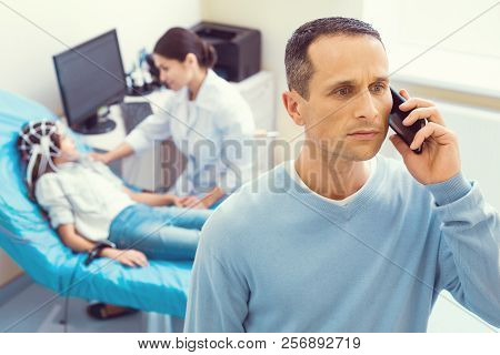 Scared Father Talking On Phone While Daughter Undergoing Electroencephalography