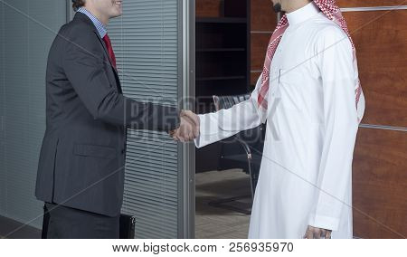 Middle Eastern And Caucasian Businessmen Shaking Hands, In An Office