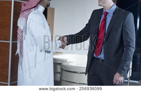 Middle Eastern And Caucasian Businessmen Shaking Hands, In An Office