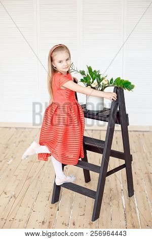 Young Little Blonde Girl Standing On Scaling-ladder Cares For Flowers