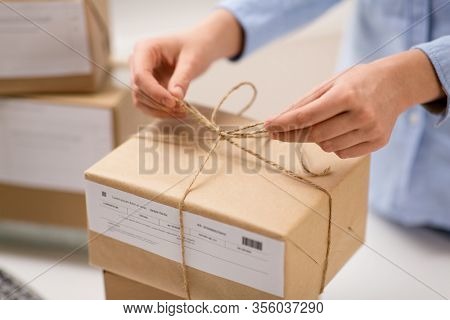 delivery, mail service, people and shipment concept - close up of woman packing parcel box and tying rope at post office