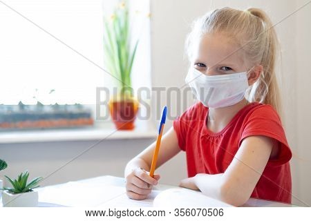 Serios Sad Blonde Schoolgirl In Medical Mask Studying At Home, Doing School Homework, Writing In Not
