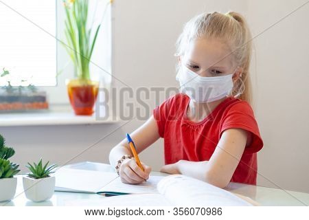 Serios Sad Blonde Schoolgirl In Medical Mask Stydying At Home, Doing School Homework, Writing In Not