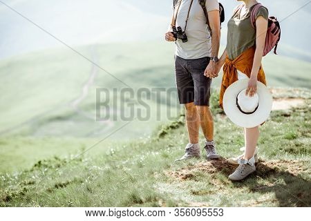 Young Couple Standing On The Green Maedow While Traveling In The Mountains During The Summer Time. C