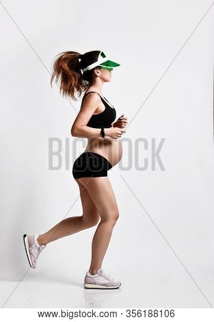 Pregnant Girl With Belly, In Green Sun Visor, Black Sport Shorts And Top, Pink Sneakers. She Is Jogg