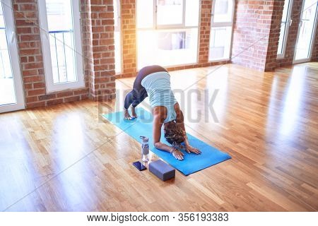 Middle age beautiful sportwoman standing on mat practicing yoga doing dolphin pose at gym