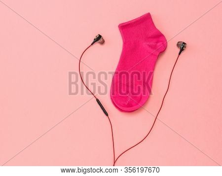 Red Sports Sock And Red Headphones On A Pink Background. The Concept Of Music And Sports. Flat Lay.
