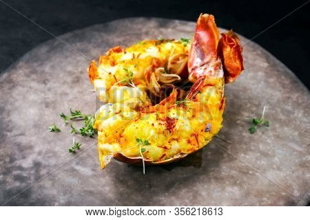 Traditional barbecue spiny lobster tail sliced and offered with saffron lemon sauce as closeup on a rustic modern design plate 