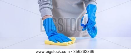 Young Woman Housekeeper In Apron Is Cleaning, Wiping Down Table Surface With Blue Gloves, Wet Yellow