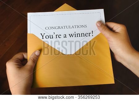 An Open Shiny Gold Envelope With A Letter That Says Congratulations You're A Winner! With Female Han