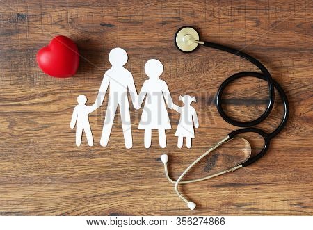 White Paper Cut Of Family, Stethoscope And Heart On Wooden Background. Health Insurance Concept.