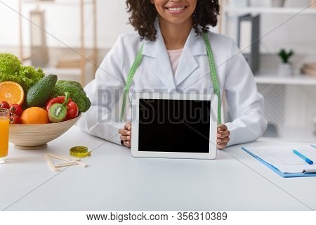 Cropped Of Black Female Doctor Dietologist Holding Digital Tablet With Blank Screen, Clinic Interior