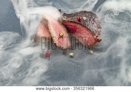 Freshly Grilled Steak With Colored Pepper On A Slate Board Wrapped In Smoke. Beef As A Main Lifestyl
