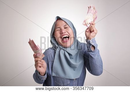 Portrait Of Indonesian Muslim Woman Holding Rupiah Money, Smiling Laughing Winning Gesture