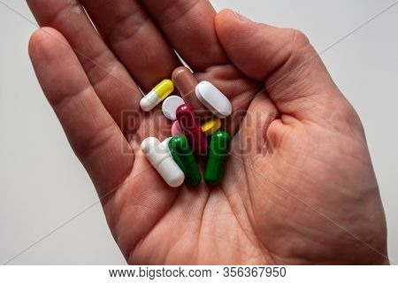 Male Hand Keeping Pills Of Diffetent Colors On White Background