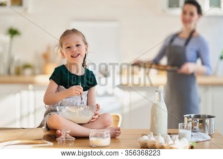 Happy loving family are preparing bakery together. Mother and child daughter girl are cooking cookies and having fun in the kitchen. Homemade food and little helper. 