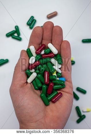 Male Hand Keeping Pills Of Diffetent Colors On White Background