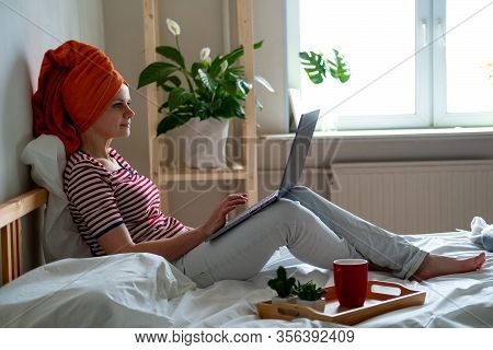Woman With Orange Towel On Head Is Working Office Work Remotely From Home On Bed. Using Computer. Di
