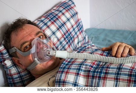 A man in an oxygen mask for CPAP therapy in bed