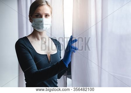 Bored woman in corona quarantine or under curfew looking out of window to the street